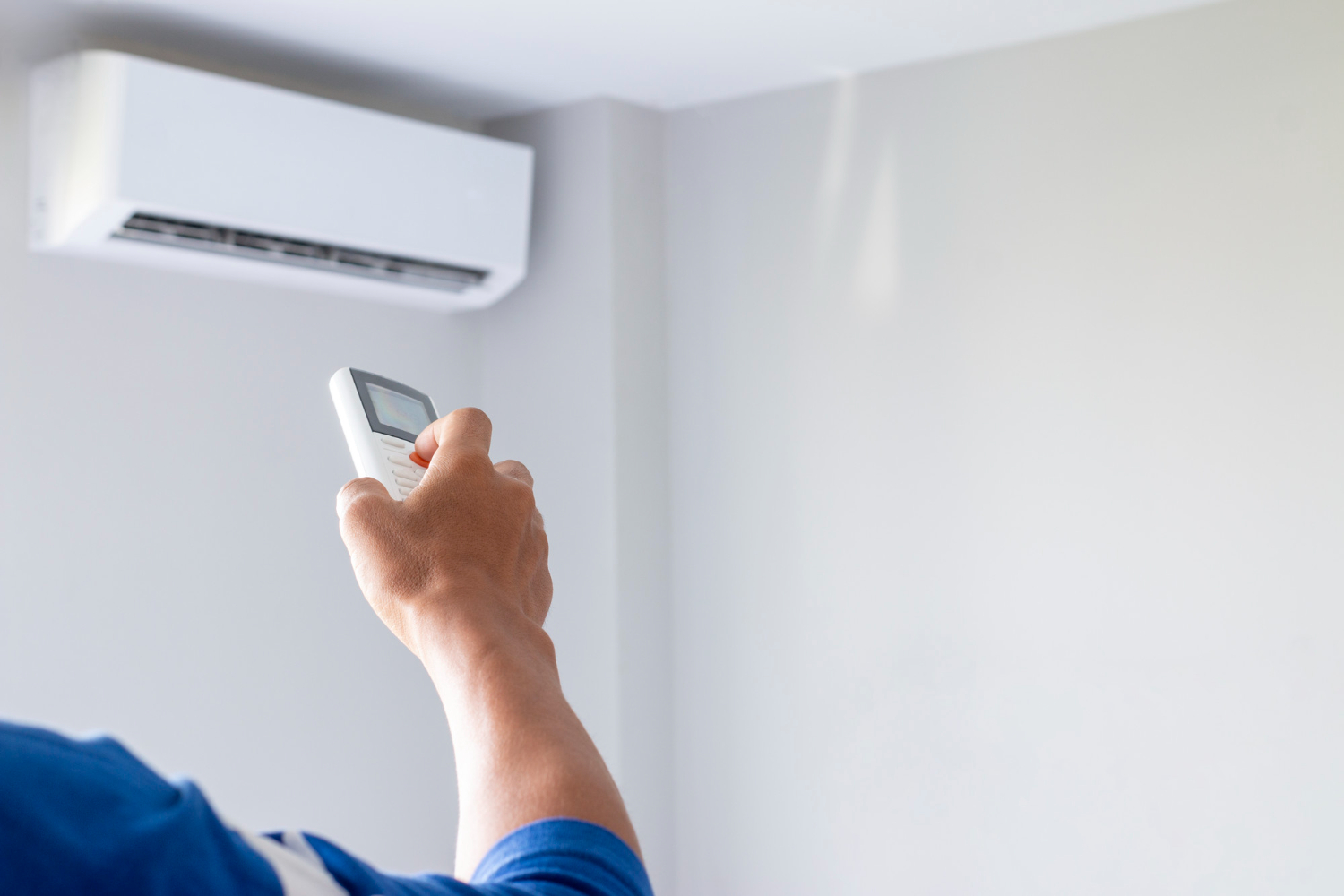 Person using remote control to adjust air conditioning unit on wall, emphasizing HVAC comfort and energy efficiency in Brookfield homes.