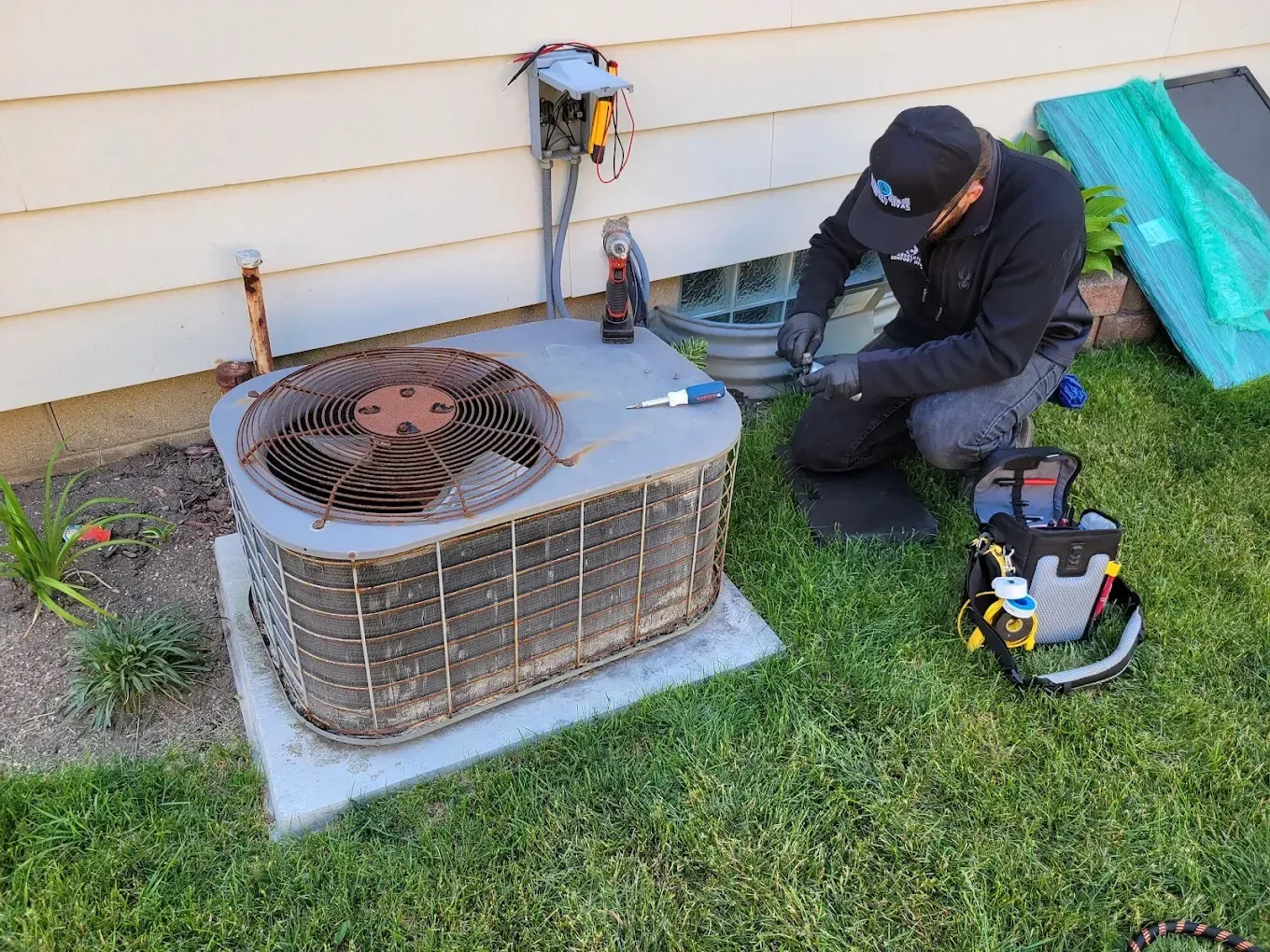 Technician servicing an outdoor air conditioning unit on grass.